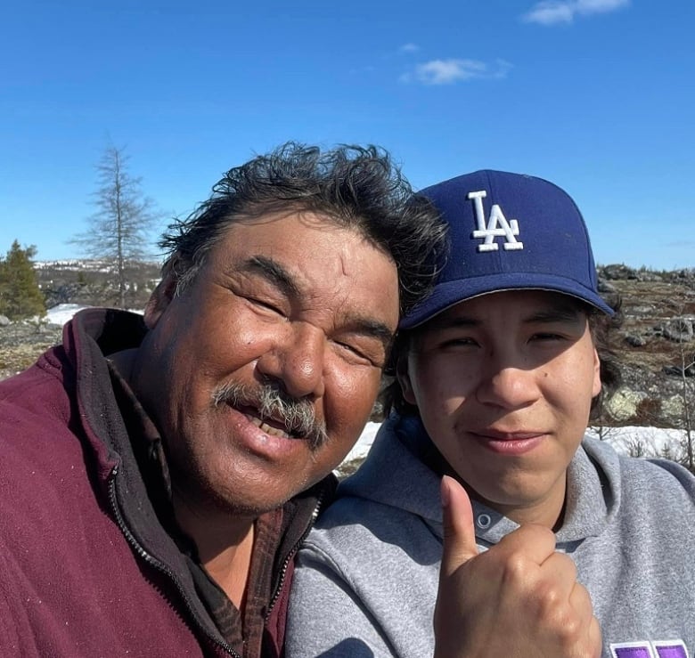 A Cree elder and his grandson smile at the camera on the land