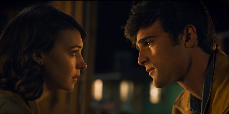 A young man and woman stare at each other, candleit film still of their profiles close up.