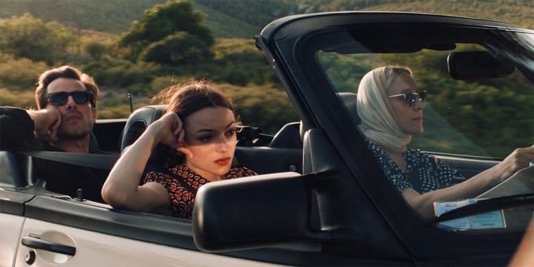 Three people sit in an open convertible.