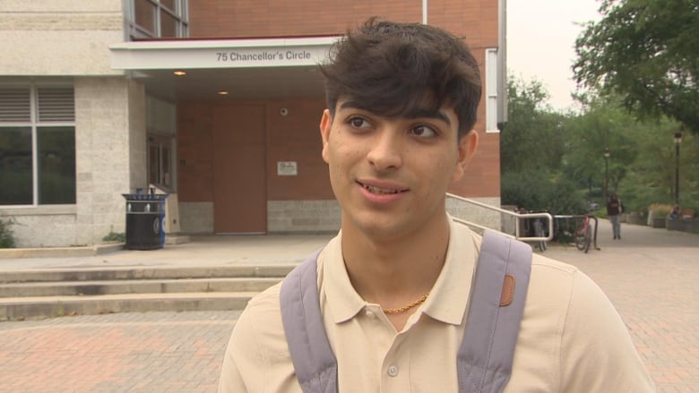 A man in a light beige shirt, wearing a light blue backpack, stands on a brick-paved road.