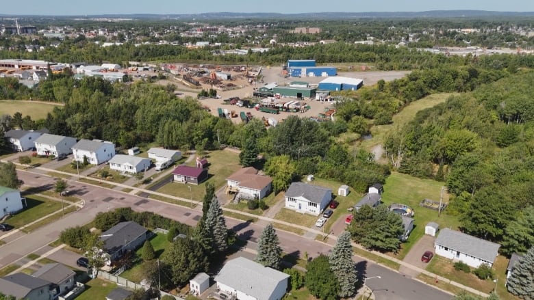 An aerial view of a residential street with trees behind houses and AIM's scrapyard beyond that.