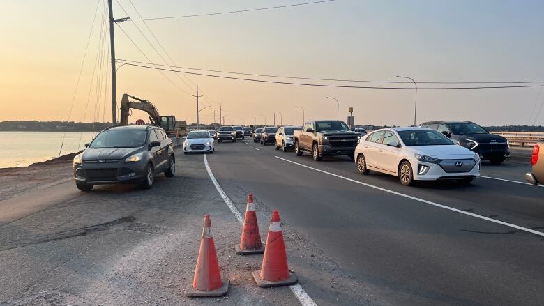 Lineups of cars crossing a bridge with orange pylons in the foreground.