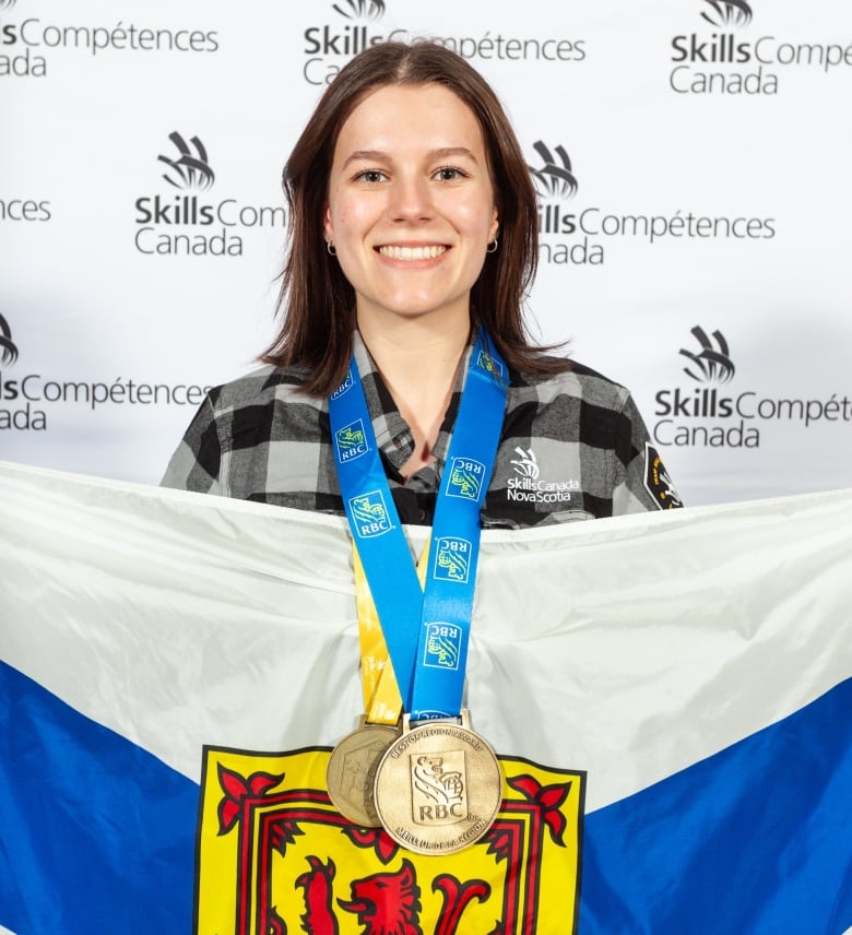 A woman holding a Nova Scotian flag, wearing gold medals, smiles for a posed photo.