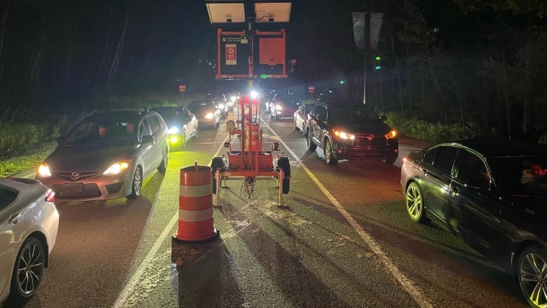 A nighttime picture of dozens of cars line up on either side of a darkened road with an orange pilon in the middle. 