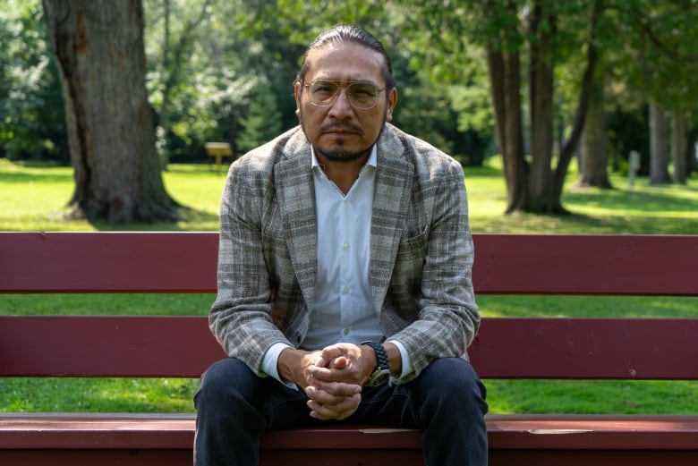 A person wearing a suit jacket sits on a red bench in a park.