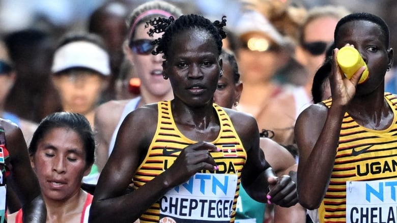 A woman in a yellow striped tank top runs at the head of a crowd 