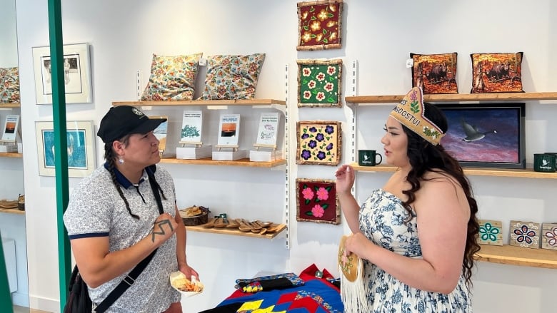 A man and a woman talk in a gallery with traditional artwork on the walls. 