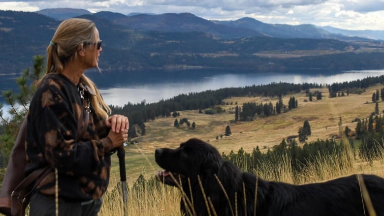 A woman stands on a hill with a big black dog.