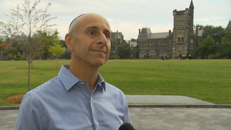 Photo of a man in a blue shirt speaking into a microphone on campus 