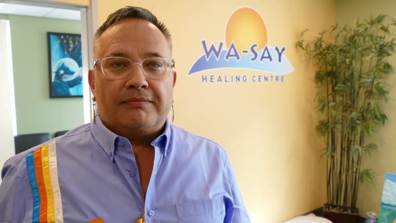 A man standing in front of wall with a logo that says 'Wa-Say Healing Centre'