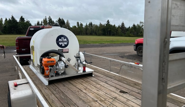 White tank with pump on flatbed trailer.