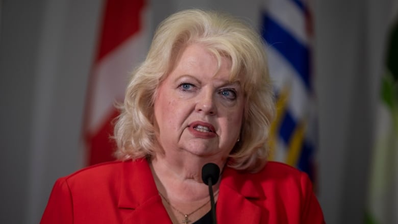 A white woman with short blond hair and a red top speaks.