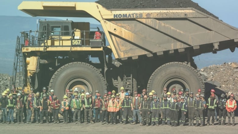 Dozens of mining workers dwarfed by a huge Komatsu dump truck at a mining site.