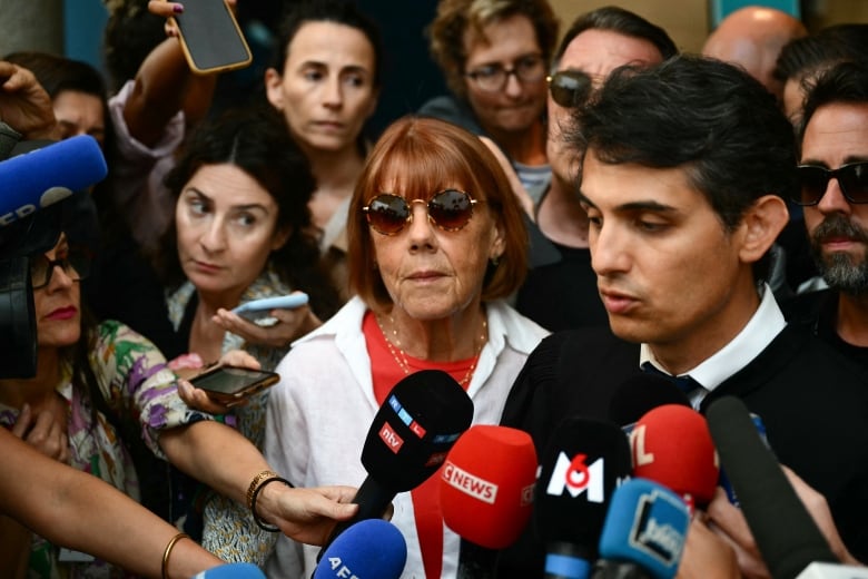 A woman in sunglasses is surrounded by press