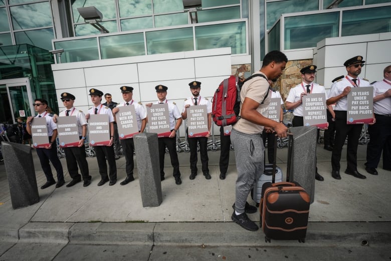 A traveller passes a line of pilots holding signs.