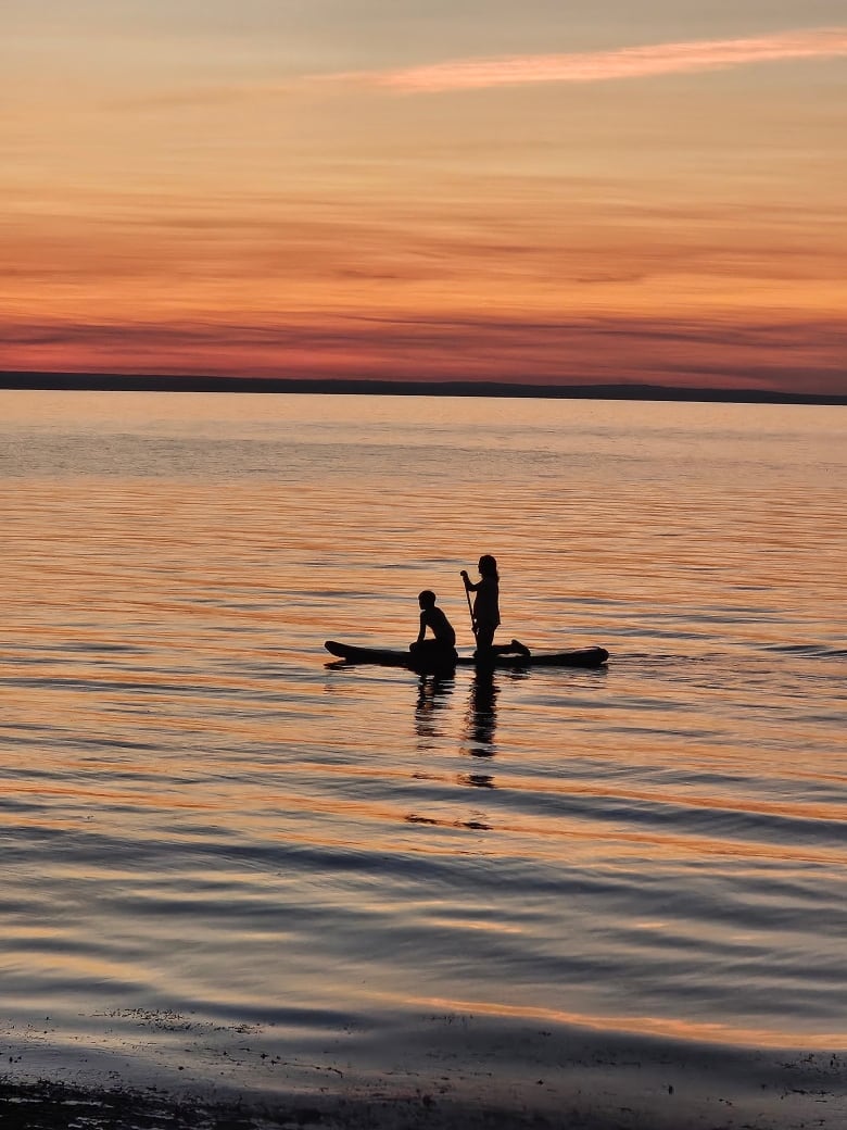 Two people paddle board over water reflecting the setting sun.