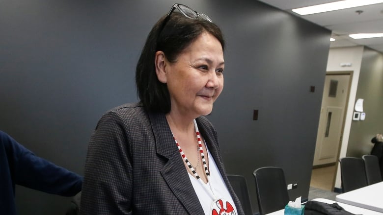 A woman with a beaded necklace stands near a table in a meeting room.