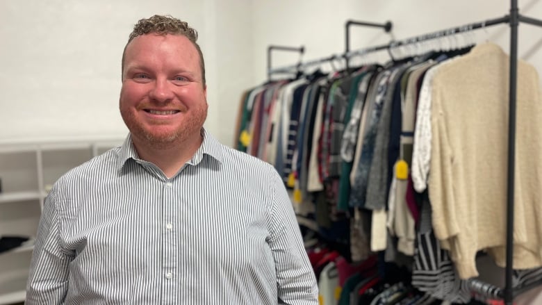 A smiling man standing in front of a rack of clothes