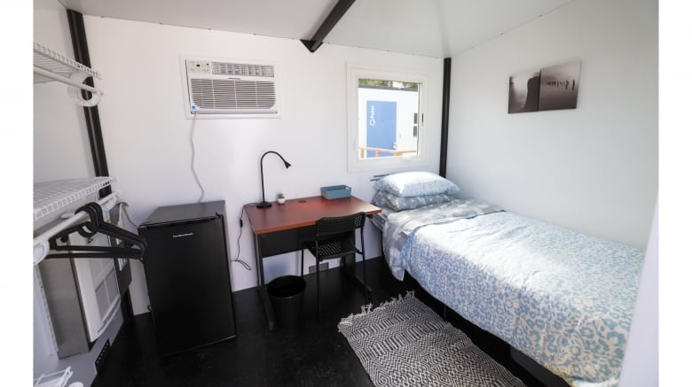 The interior of a small room, with a single bed, a small desk and a small refrigerator.