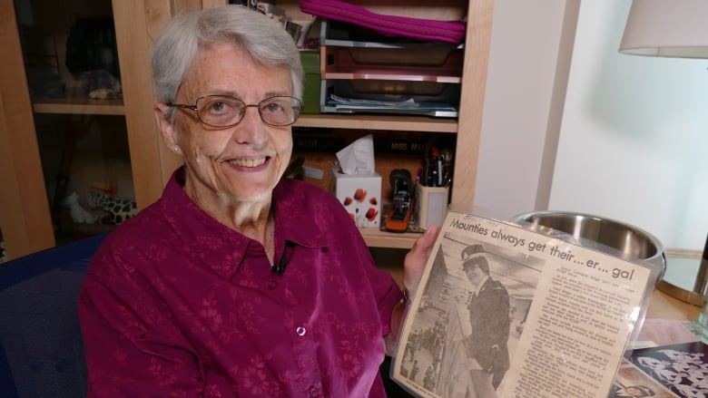 Woman on a purple shirt hold an old, laminated newspaper.