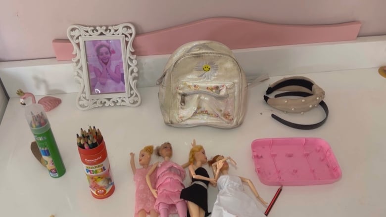 A framed picture, colouring crayons and some barbies lay on a desk