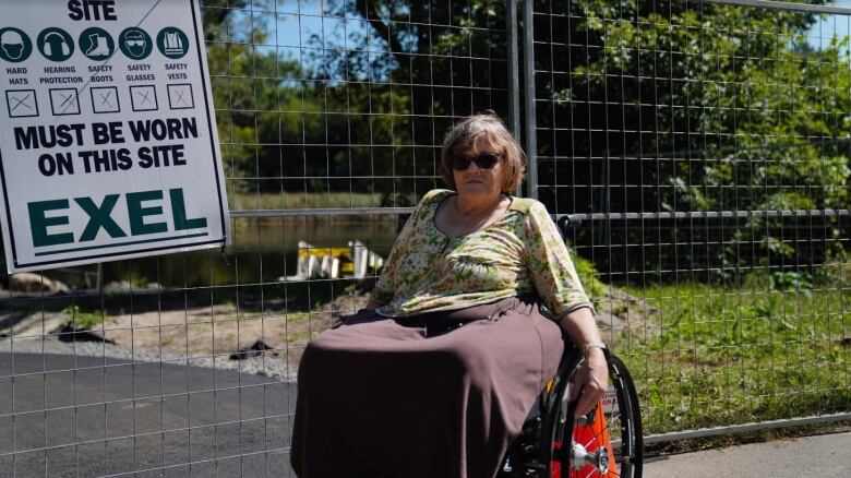 a woman posing in her wheelchair outside of a construction zone of a dock which she won't be able to safely access