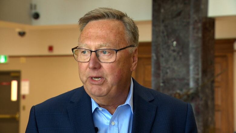 A man wearing a blazer and blue shirt stands in the lobby of Confederation Building.