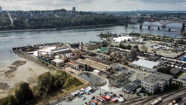 A sprawling industrial complex borders a body of water next to a bridge.