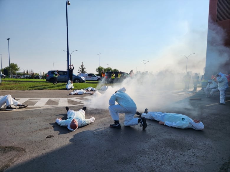 People lay on the ground in white with smoke around them.