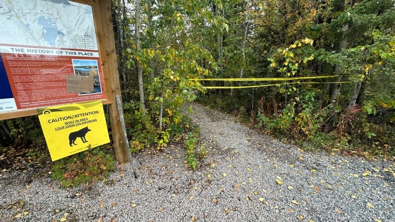 Yellow caution tape stretches across a trail head. On a nearby sign, a notice warns people of a wolf in the area.