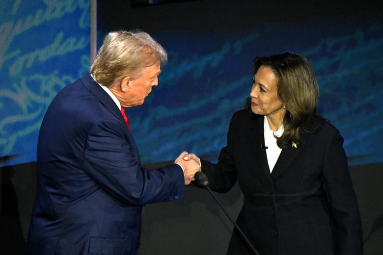 A man and a woman in suits shake hands behind a podium.