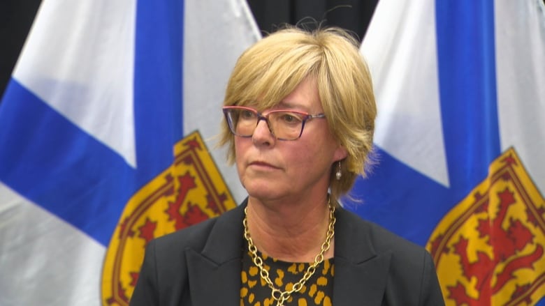 A woman stands in front of two Nova Scotia flags.