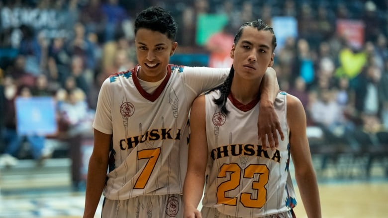 Two male basketball players stand on a court.