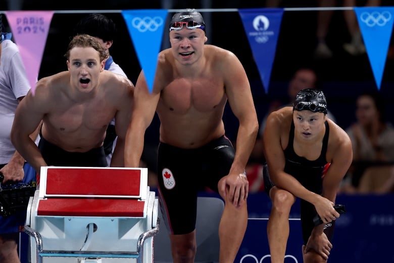 Three swimmers watch a race from the pool deck.