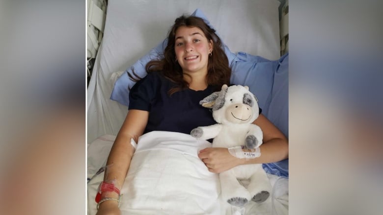 A girl lies in a hospital bed clutching a stuffed animal. 