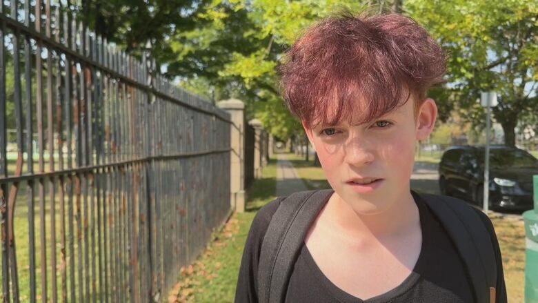 A boy stands on a sidewalk outside.