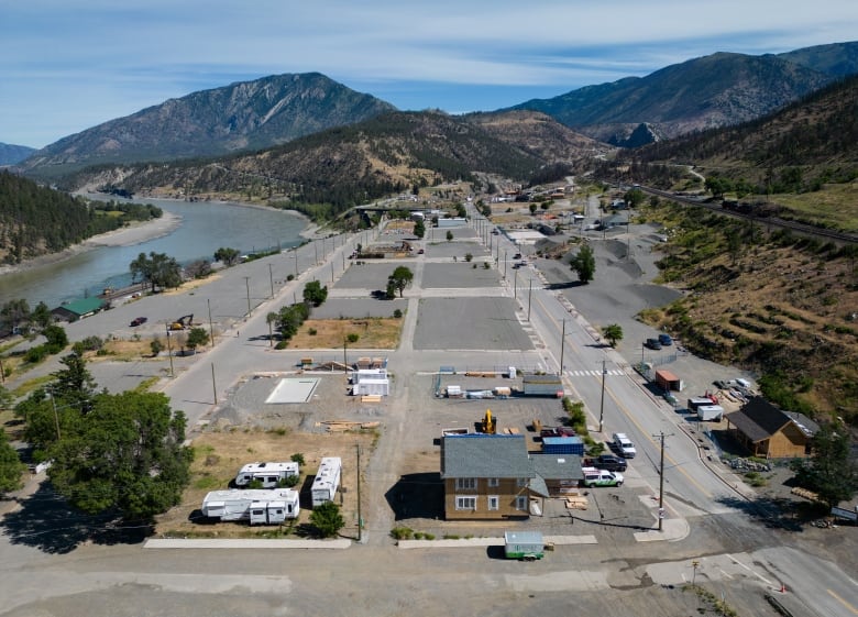 An aerial picture of a town with empty lots, framed by mountains and a river.