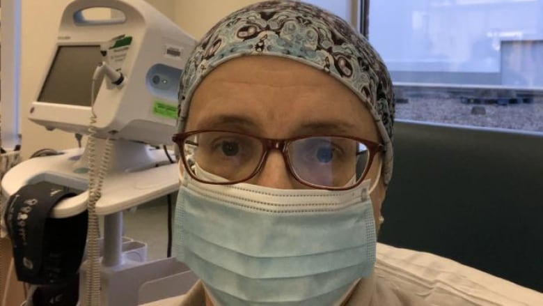 A woman in glasses, a surgical mask and a turban looks at the camera. 