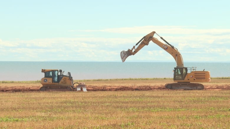 Construction machinery is seen working with water on the horizon.  