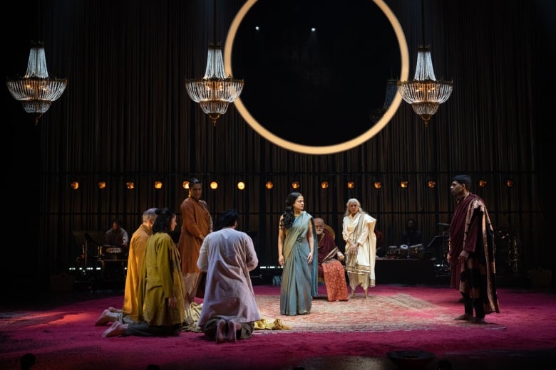 A group of men and women stand in a circle around a woman wearing a blue sari. 