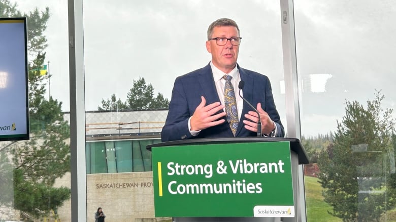 A man in a suit with glasses speaks at a podium.