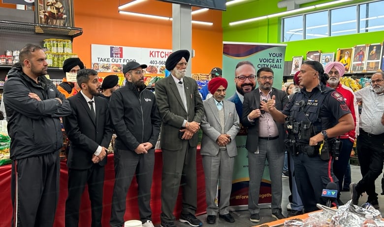 A police officer speaks to a group of men in a grocery store at a meeting.