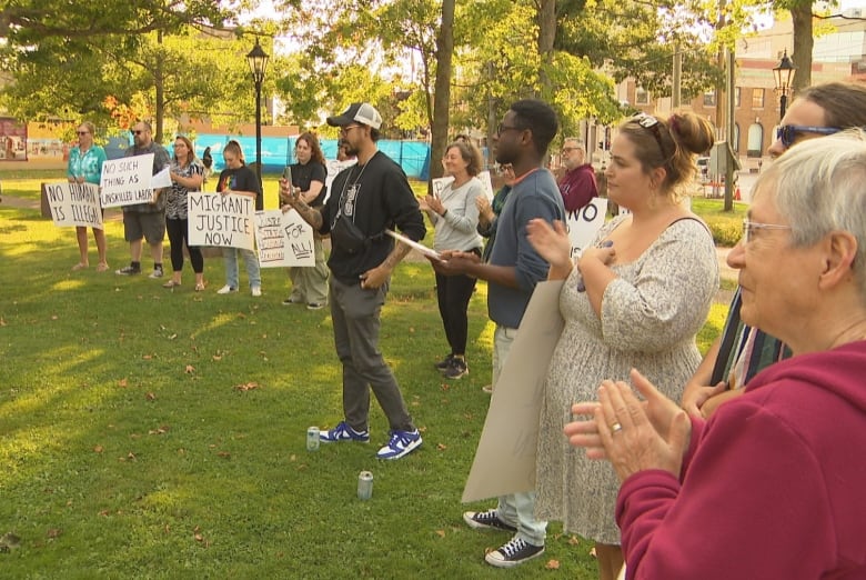 Protestors hold up signs and applaud on a lawn outside Province House.