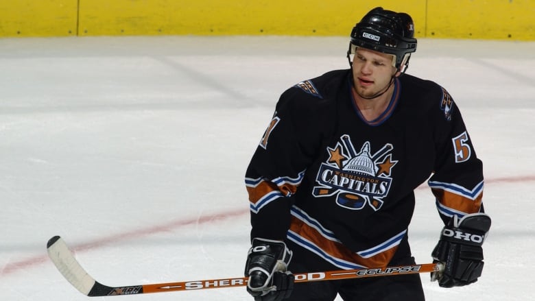 A men's hockey player watches the play as he holds his stick with two hands.