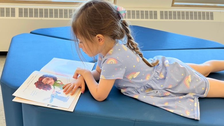 A young girl in a blue dress with rainbows on it reads a French picture book