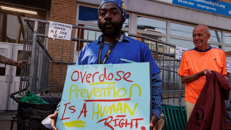 Photo of a man holding a sign reading, 'overdose prevention is a human right.' 