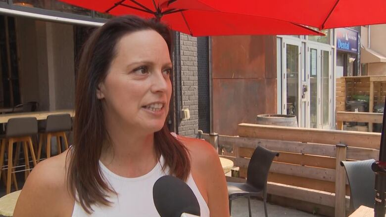 Woman in a white shirt speaking into a microphone outside