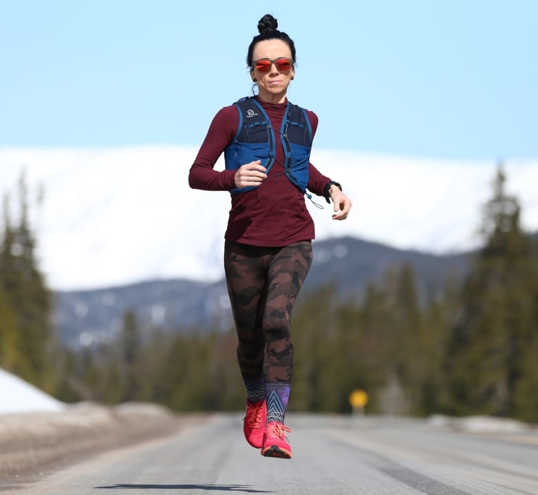 A woman appears to be suspended in mid-air while running. She's in mid-stride as she runs down a road.