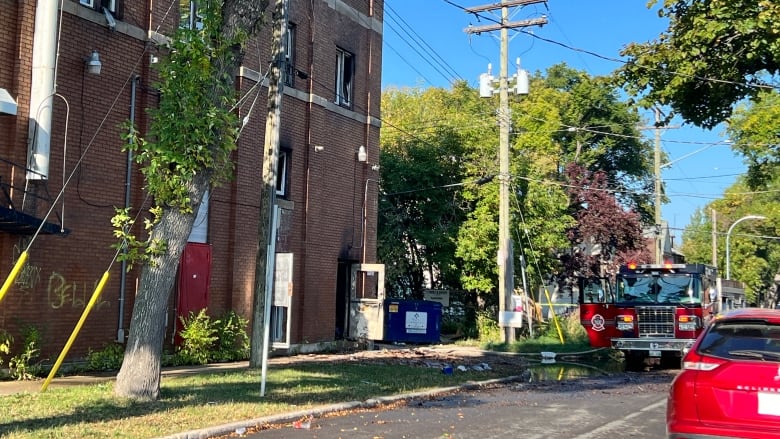 A fire truck is parked outside a building that was on fire. Some of the windows in the building are smashed and the back door is open. 