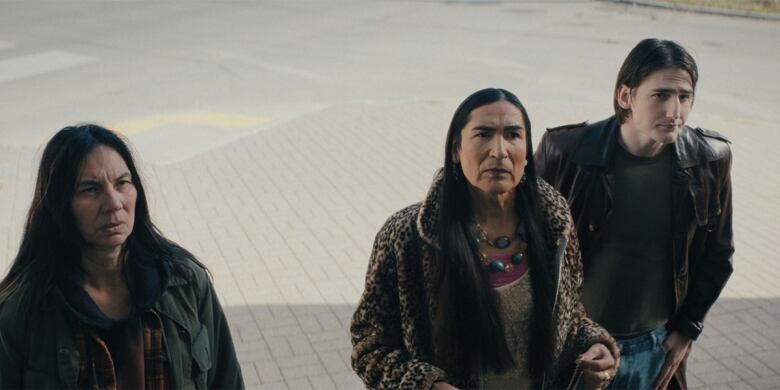 A still from a film shows three people standing on a city sidewalk looking upward.